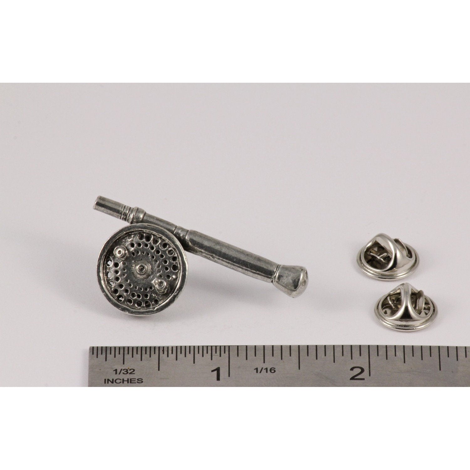 A handcrafted Saltwater Fly Rod Reel Pin next to a ruler, available for sale at Creativeartisan.com - the image offers a sense of scale