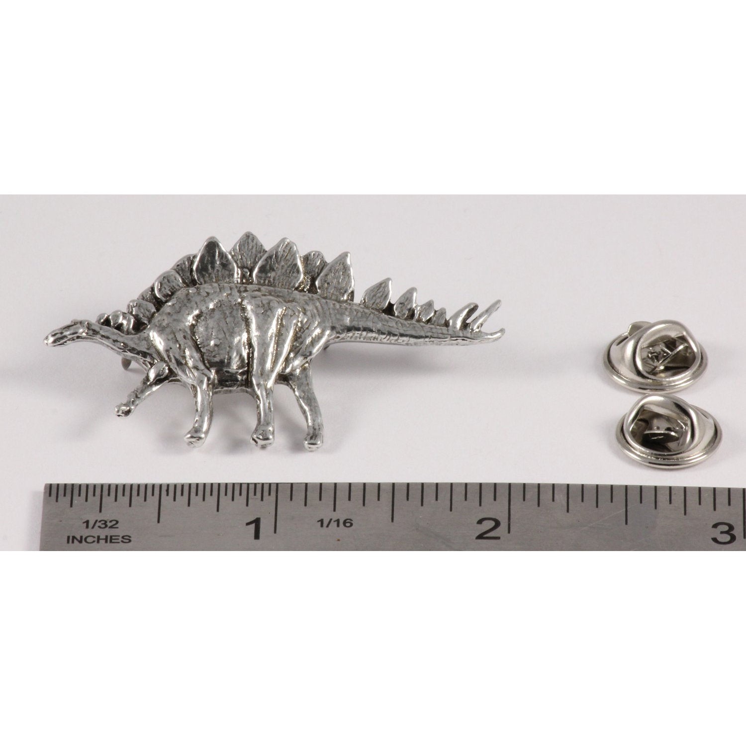 A handcrafted Stegosaurus Pin next to a ruler, available for sale at Creativeartisan.com - the image offers a sense of scale