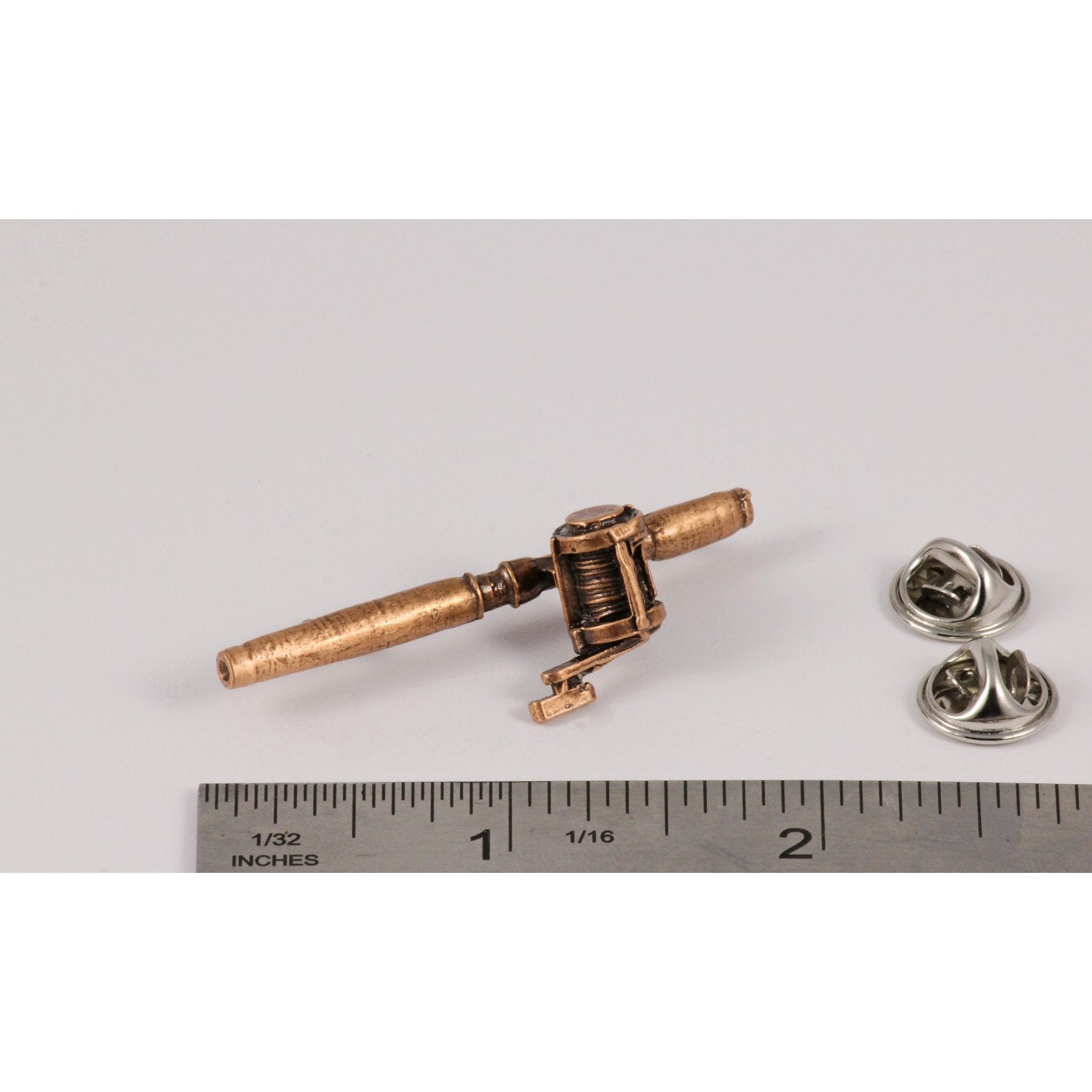 A handcrafted Bait Casting Rod Reel Pin next to a ruler, available for sale at Creativeartisan.com - the image offers a sense of scale
