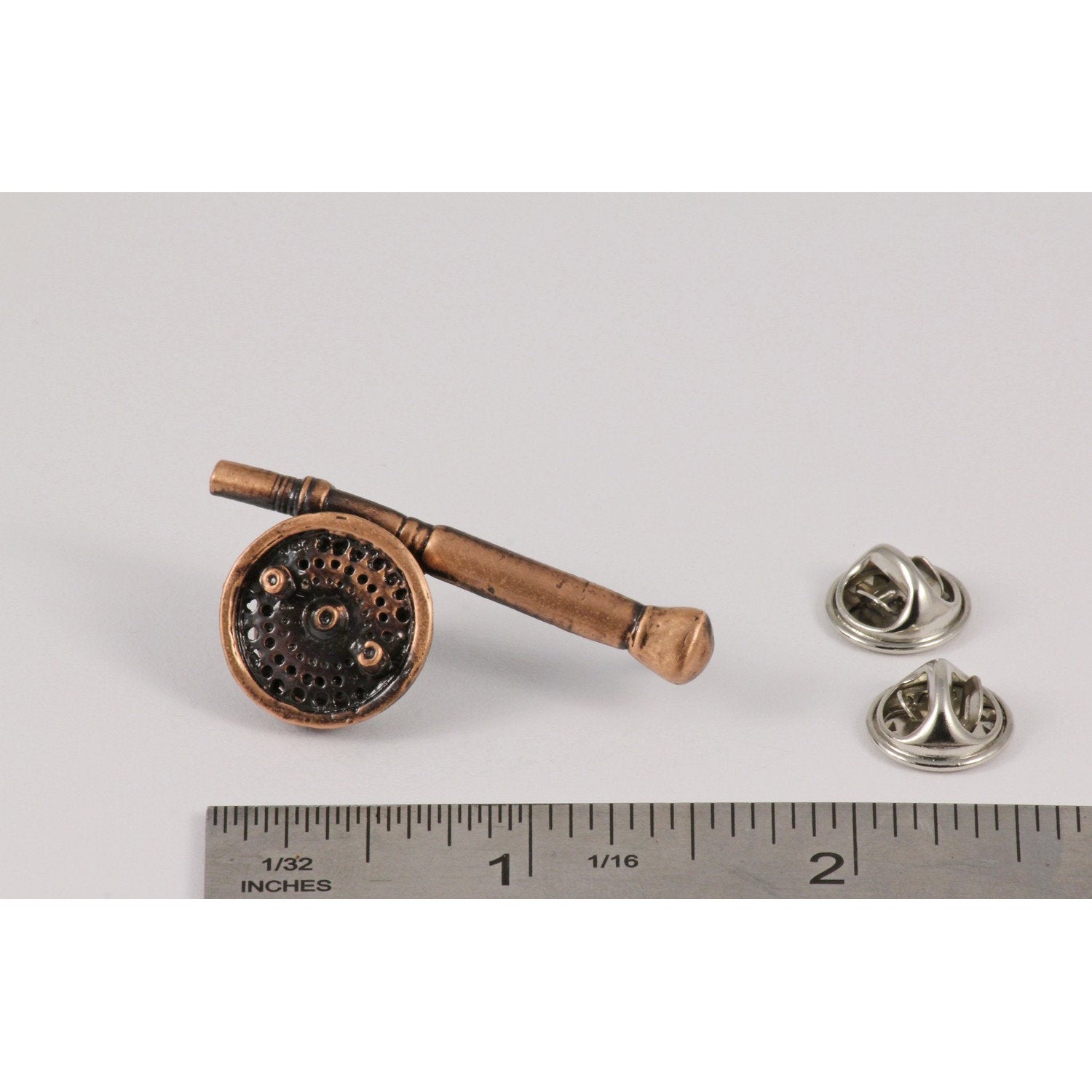 A handcrafted Saltwater Fly Rod Reel Pin next to a ruler, available for sale at Creativeartisan.com - the image offers a sense of scale