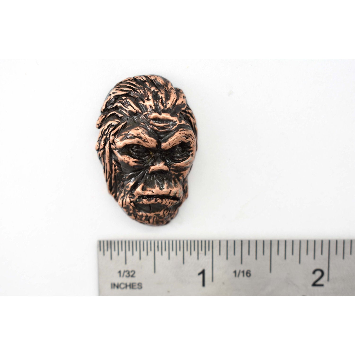 A handcrafted Sasquatch Bigfoot Head Pin next to a ruler, available for sale at Creativeartisan.com - the image offers a sense of scale