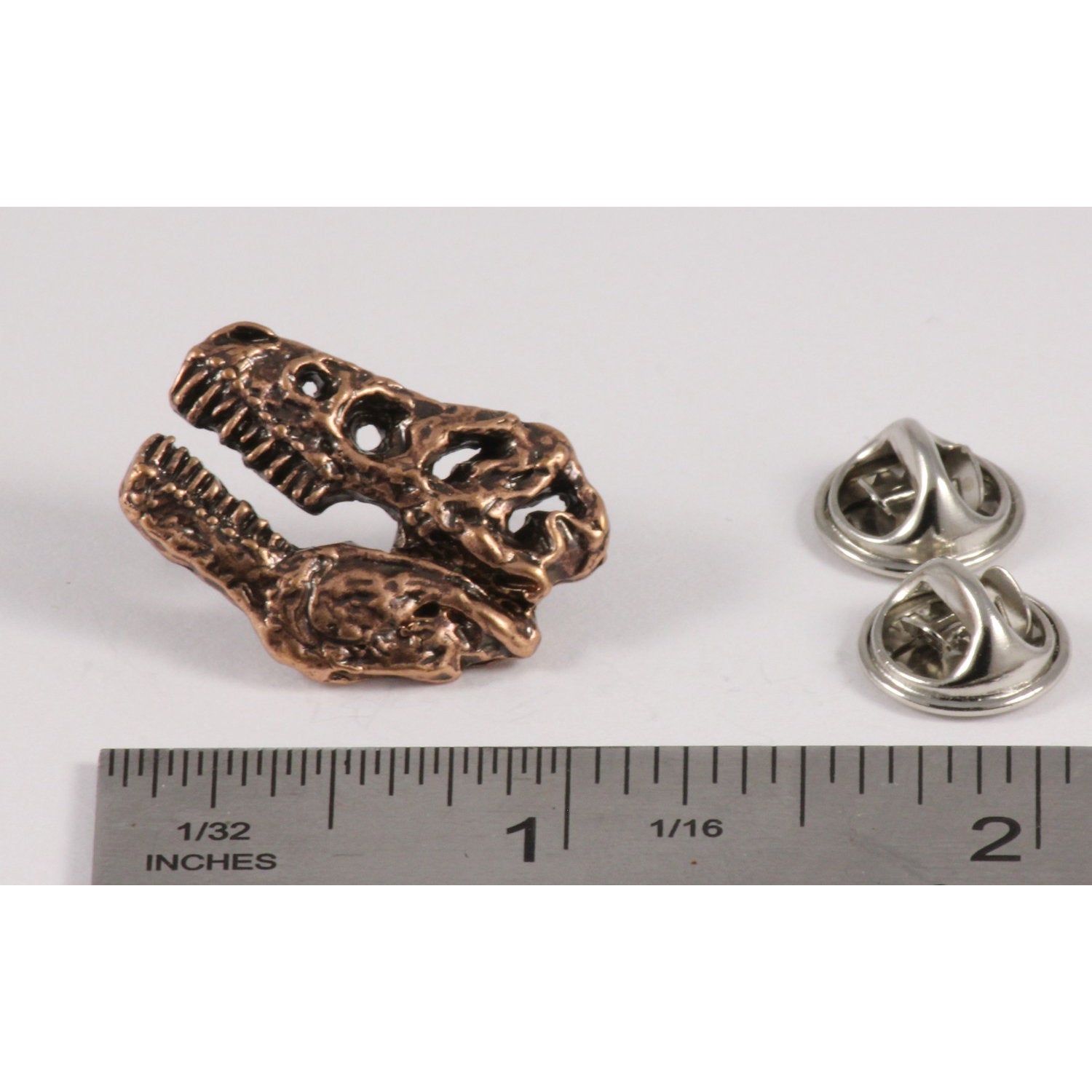 A handcrafted Tyrannosaurus Rex Fossilized Head Pin next to a ruler, available for sale at Creativeartisan.com - the image offers a sense of scale