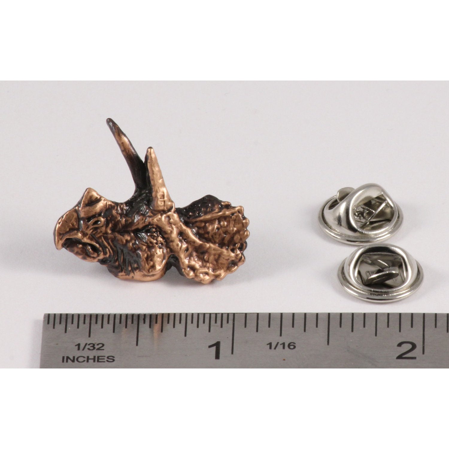 A handcrafted Triceratops Head Pin next to a ruler, available for sale at Creativeartisan.com - the image offers a sense of scale