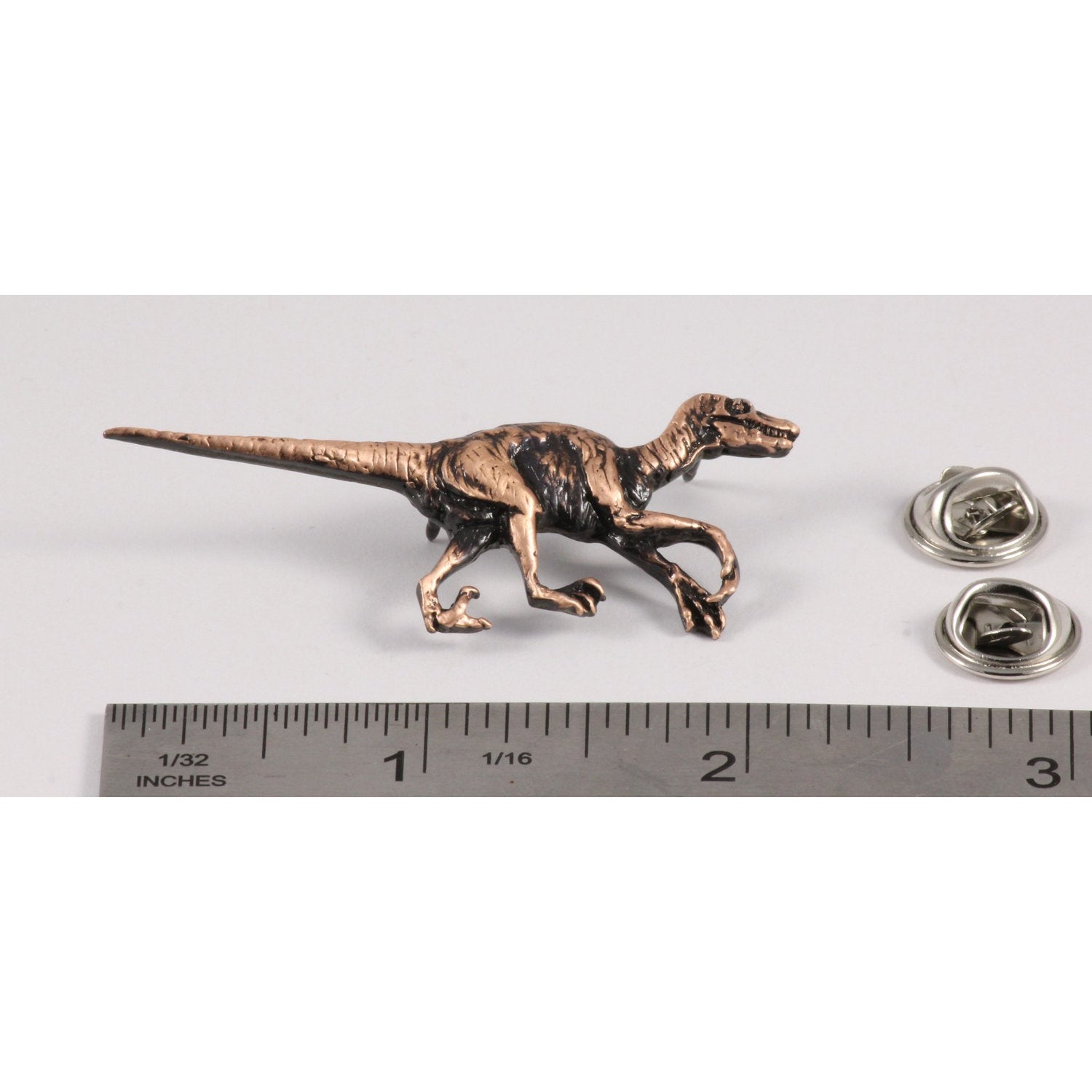 A handcrafted Velociraptor Pin next to a ruler, available for sale at Creativeartisan.com - the image offers a sense of scale