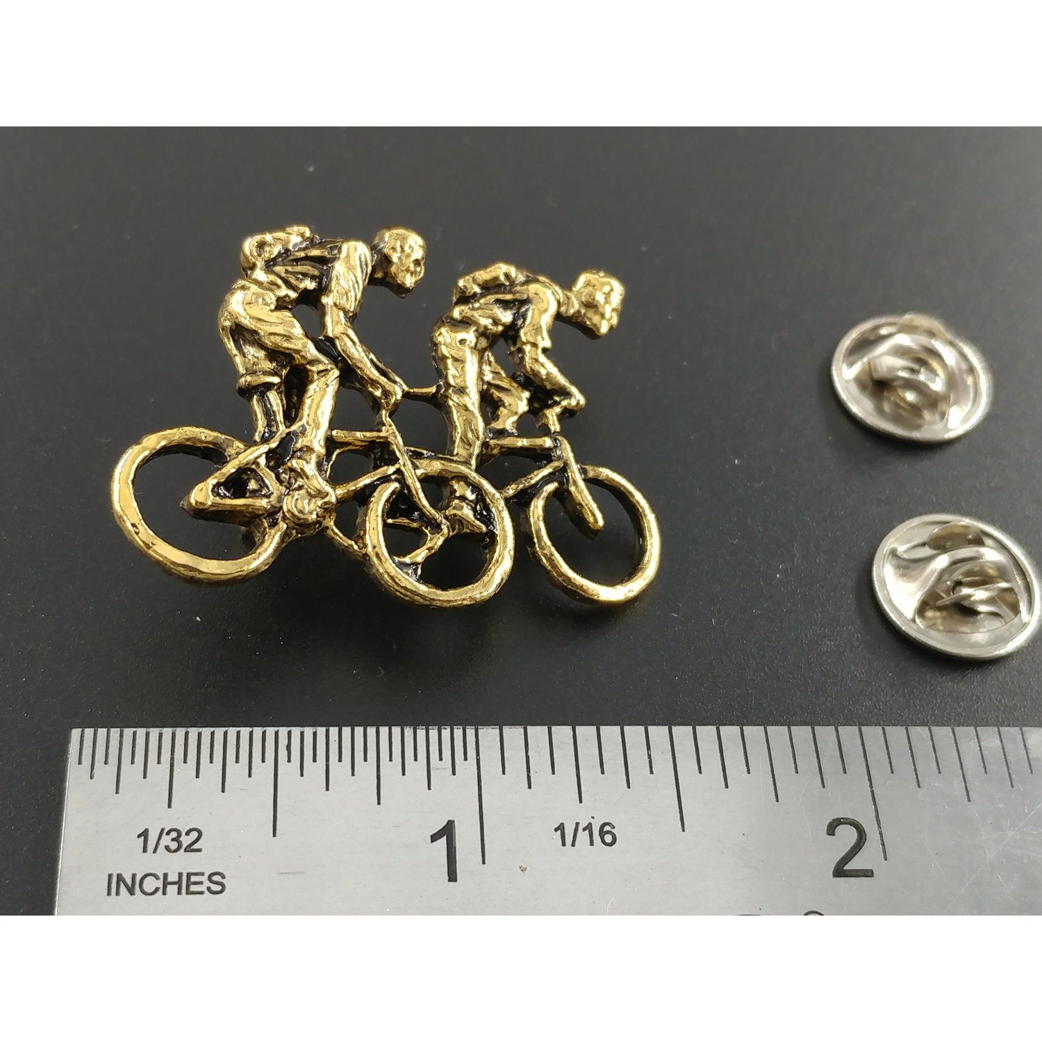 A handcrafted Two Bicyclers Pin next to a ruler, available for sale at Creativeartisan.com - the image offers a sense of scale